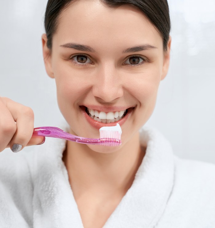 woman-holding-pink-toothbrush-with-toothpaste-bathroom